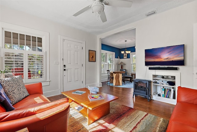 living room featuring dark hardwood / wood-style flooring, ceiling fan with notable chandelier, and a wood stove