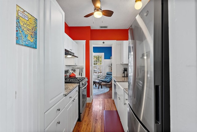 kitchen featuring appliances with stainless steel finishes, tasteful backsplash, white cabinetry, hardwood / wood-style flooring, and light stone countertops