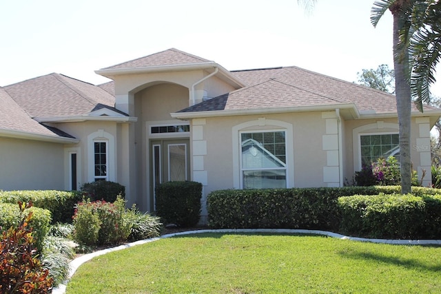 view of front facade with a shingled roof, a front yard, and stucco siding