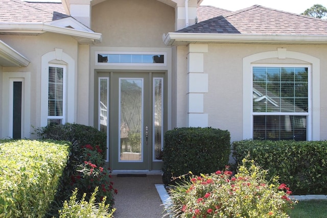 view of exterior entry featuring a shingled roof and stucco siding