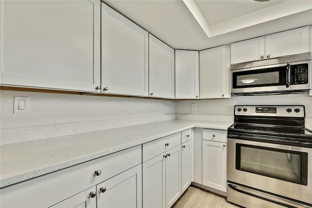 kitchen featuring light stone countertops, appliances with stainless steel finishes, white cabinets, and light hardwood / wood-style flooring