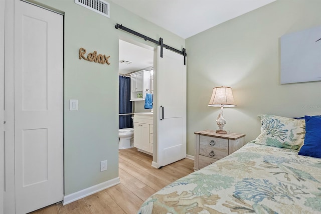 bedroom featuring light wood finished floors, a barn door, visible vents, and baseboards