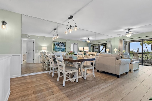 dining area with light wood-style floors, a ceiling fan, visible vents, and a wainscoted wall