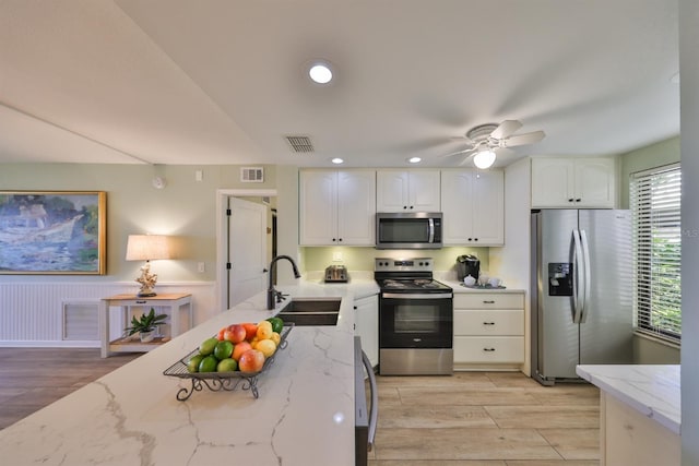 kitchen featuring visible vents, white cabinets, light stone countertops, stainless steel appliances, and a sink