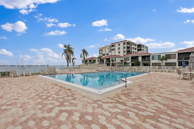 community pool featuring a patio, a water view, and fence