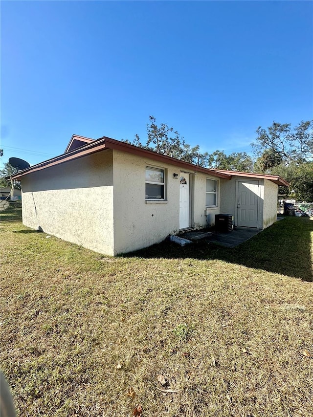 back of property featuring central AC unit, a lawn, and stucco siding