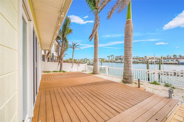 wooden terrace with a water view, fence, and a dock