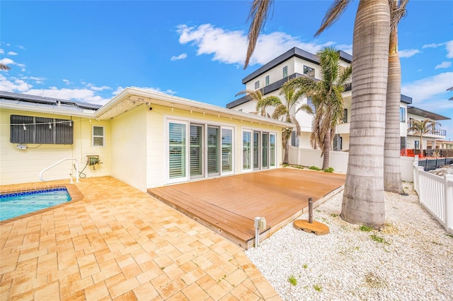 rear view of property with stucco siding, a deck, an outdoor pool, a fenced backyard, and solar panels