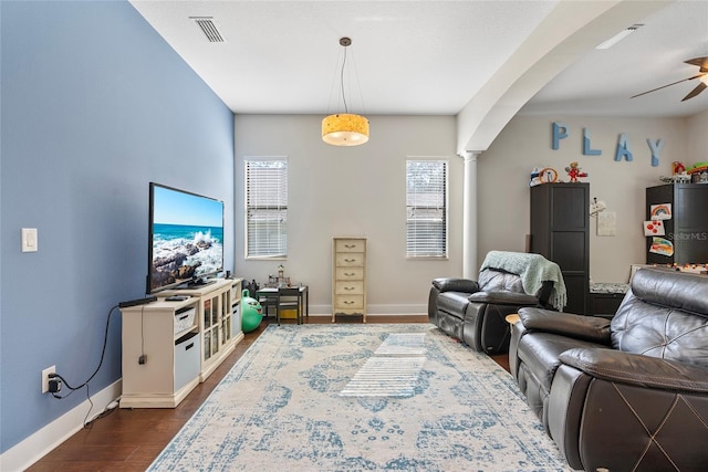 living area featuring baseboards, visible vents, arched walkways, dark wood-type flooring, and ornate columns