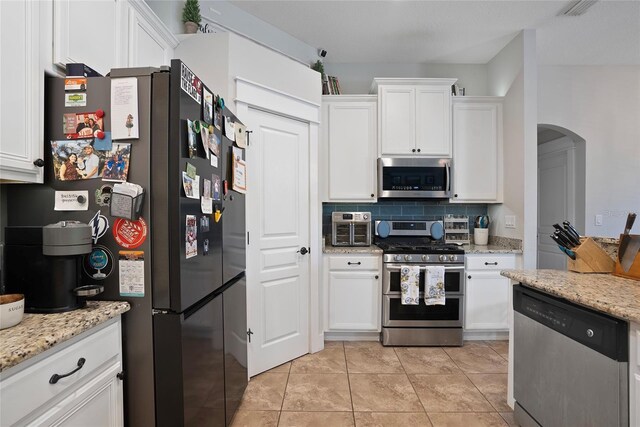 kitchen featuring arched walkways, stainless steel appliances, tasteful backsplash, white cabinets, and light tile patterned flooring