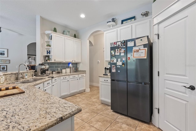 kitchen featuring arched walkways, a sink, white cabinetry, freestanding refrigerator, and open shelves