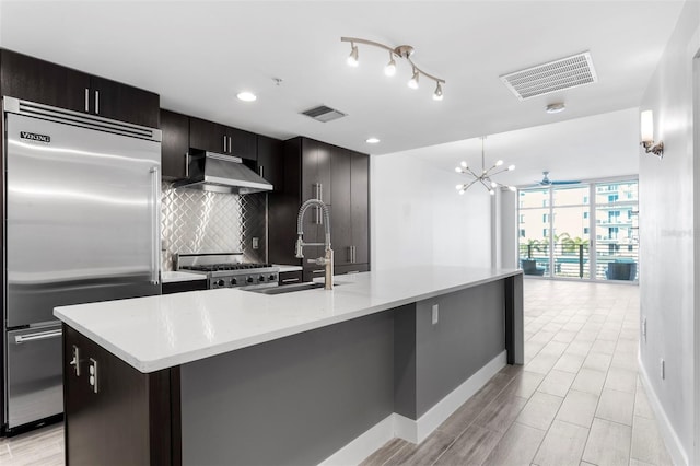 kitchen with tasteful backsplash, an island with sink, stainless steel built in fridge, and range