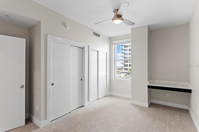 unfurnished bedroom with multiple closets, visible vents, carpet flooring, and baseboards