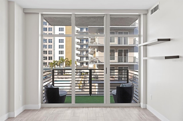 doorway with baseboards, visible vents, wood finished floors, and expansive windows