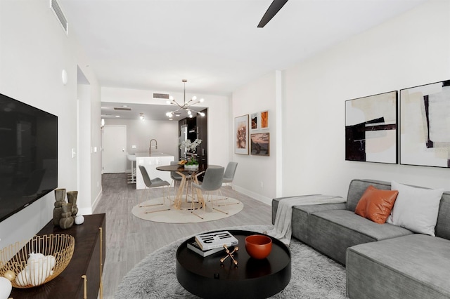 living area featuring visible vents, wood finished floors, a chandelier, and baseboards