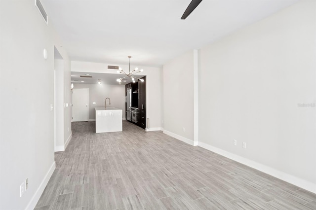 unfurnished living room featuring a notable chandelier, baseboards, and light wood-type flooring