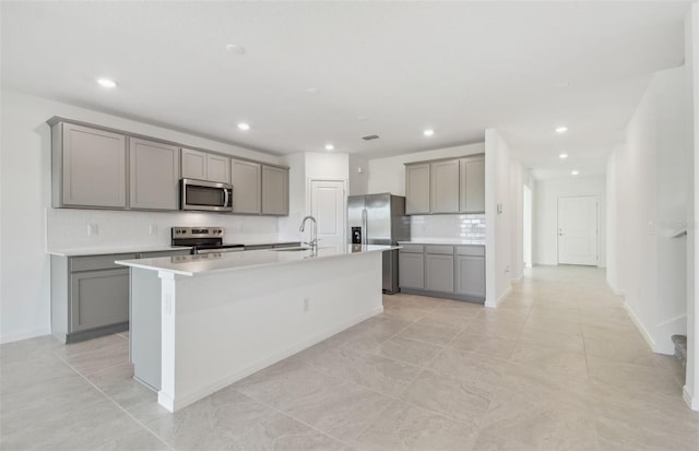 kitchen featuring a sink, appliances with stainless steel finishes, an island with sink, and gray cabinets