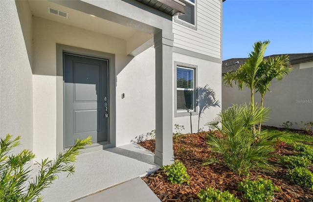 entrance to property featuring visible vents and stucco siding