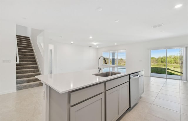 kitchen with a kitchen island with sink, a sink, open floor plan, light countertops, and stainless steel dishwasher