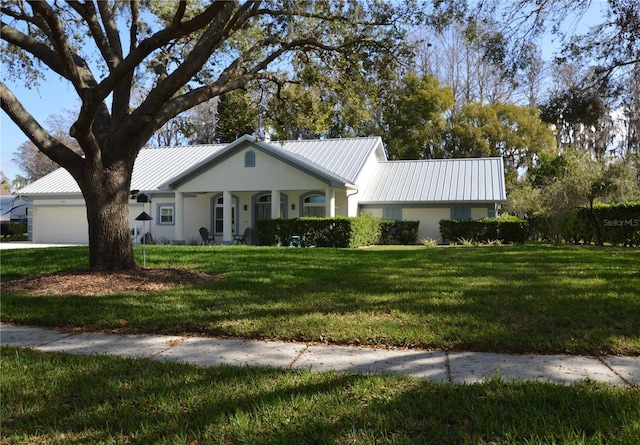 ranch-style home with an attached garage, metal roof, a front lawn, and stucco siding