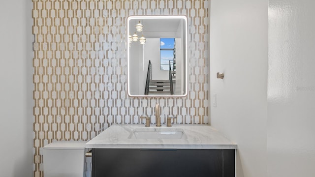 bathroom featuring toilet, vanity, and wallpapered walls