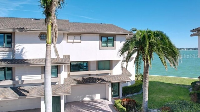 view of front of house with stucco siding, a shingled roof, a water view, a garage, and driveway