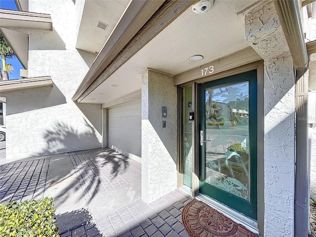 doorway to property featuring a garage, driveway, and stucco siding