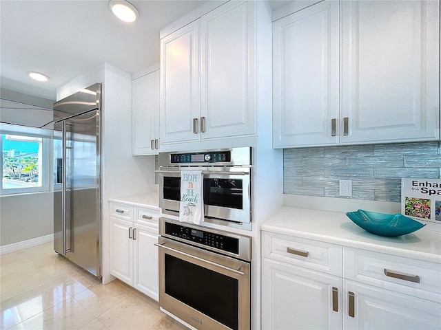 kitchen with appliances with stainless steel finishes, white cabinets, light countertops, and backsplash