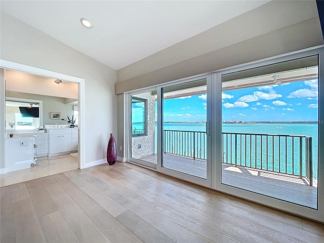 doorway featuring light wood-type flooring, a water view, vaulted ceiling, and baseboards