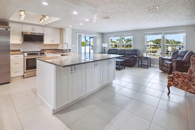 kitchen featuring sink, appliances with stainless steel finishes, white cabinetry, dark stone countertops, and a textured ceiling