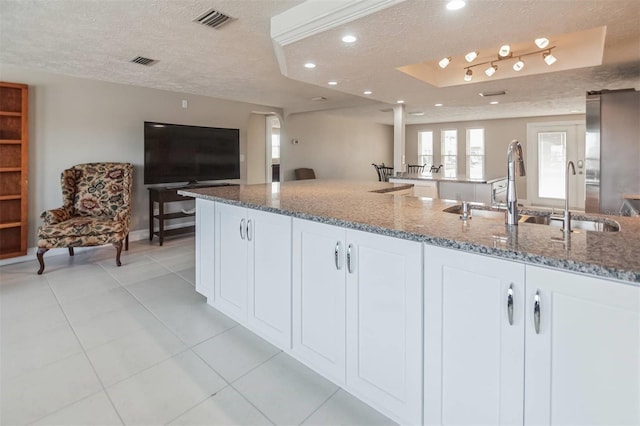 kitchen with a raised ceiling, dark stone countertops, white cabinets, and a textured ceiling