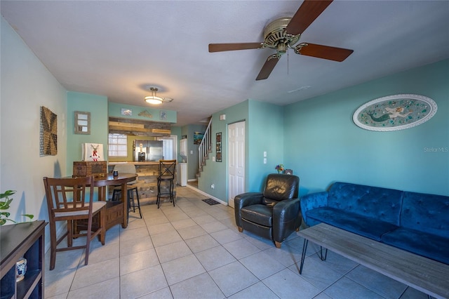 living area with a ceiling fan, stairway, baseboards, and light tile patterned floors