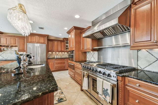 kitchen with high end appliances, hanging light fixtures, ventilation hood, and dark stone countertops