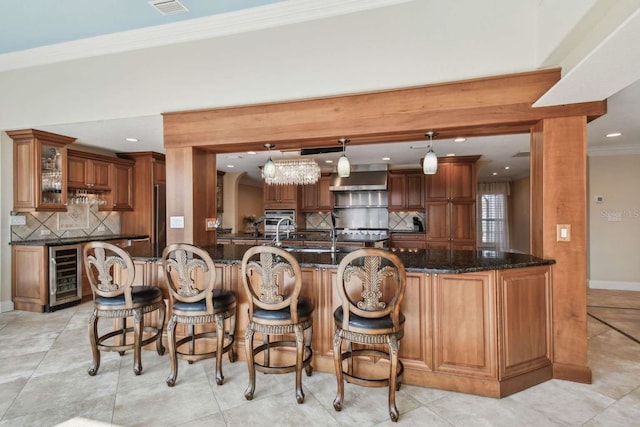 kitchen featuring crown molding, tasteful backsplash, hanging light fixtures, dark stone counters, and beverage cooler