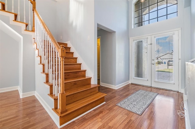 foyer entrance featuring wood-type flooring, a towering ceiling, and french doors