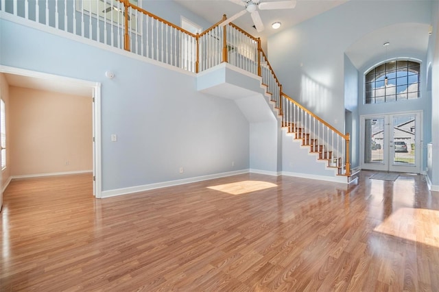 unfurnished living room featuring a towering ceiling, light hardwood / wood-style flooring, french doors, and ceiling fan