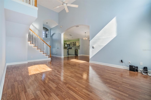 unfurnished living room with a towering ceiling, wood-type flooring, and ceiling fan with notable chandelier