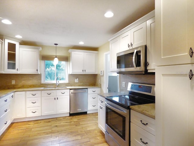 kitchen featuring sink, stainless steel appliances, white cabinets, decorative light fixtures, and light wood-type flooring