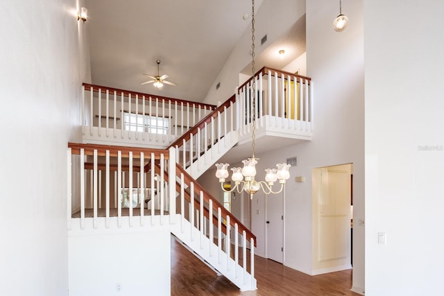 stairs with a high ceiling, hardwood / wood-style flooring, and ceiling fan with notable chandelier