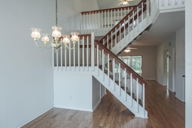 stairs with hardwood / wood-style flooring, ceiling fan with notable chandelier, and a high ceiling