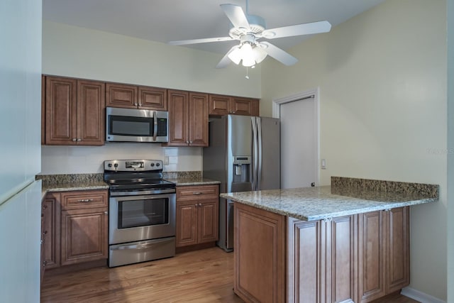 kitchen featuring light stone countertops, appliances with stainless steel finishes, ceiling fan, and light hardwood / wood-style floors