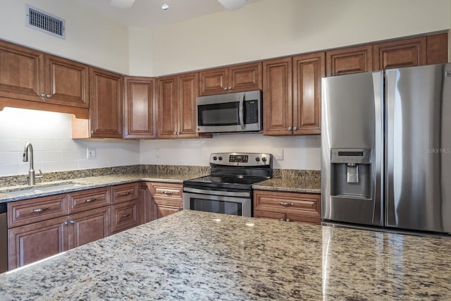 kitchen featuring stainless steel appliances, light stone countertops, sink, and decorative backsplash