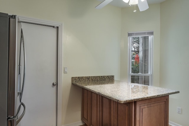 kitchen featuring stainless steel refrigerator, ceiling fan, and light stone countertops