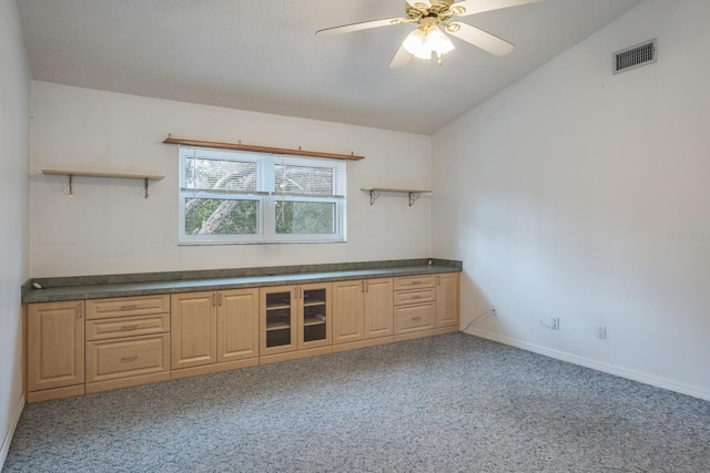 interior space with ceiling fan, lofted ceiling, light brown cabinetry, and carpet floors