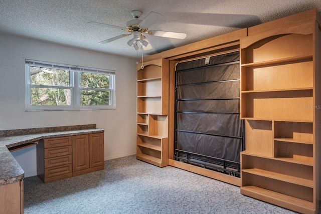 unfurnished office featuring ceiling fan, light carpet, built in desk, and a textured ceiling