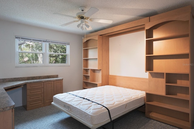 bedroom with ceiling fan, dark carpet, built in desk, and a textured ceiling