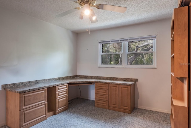 unfurnished office with a textured ceiling, built in desk, light colored carpet, and ceiling fan