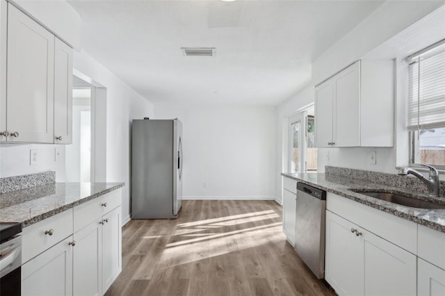 kitchen with stainless steel appliances, white cabinetry, light stone countertops, and sink