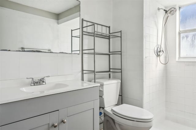 bathroom featuring tiled shower, vanity, toilet, and tile walls