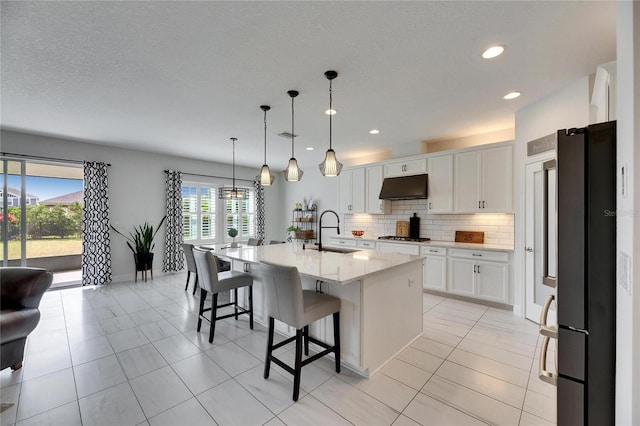 kitchen featuring a breakfast bar area, stainless steel appliances, decorative backsplash, a sink, and under cabinet range hood